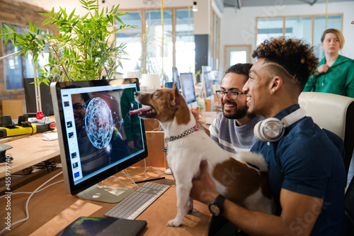 Man holding dog, sitting at computer with colleague photo