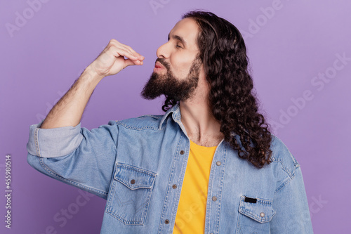 Profile portrait of bearded man gourmet gesture fingers lips on purple wall