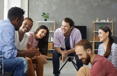 Young mixed race people having fun and enjoying good time together. Diverse group of six happy millennial friends sitting on the sofa in the living-room and laughing at a funny joke photo