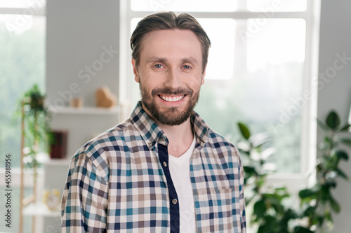 Portrait of attractive cheerful content guy wearing checked shirt staying home light white room indoors