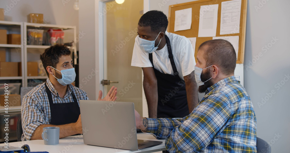 Small business owners in safety mask discuss strategy on laptop in warehouse Small business owners in safety mask discuss strategy on laptop in warehouse
