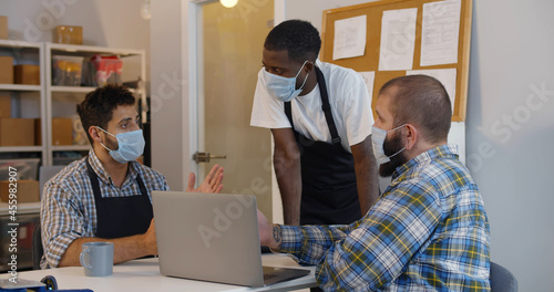 Small business owners in safety mask discuss strategy on laptop in warehouse