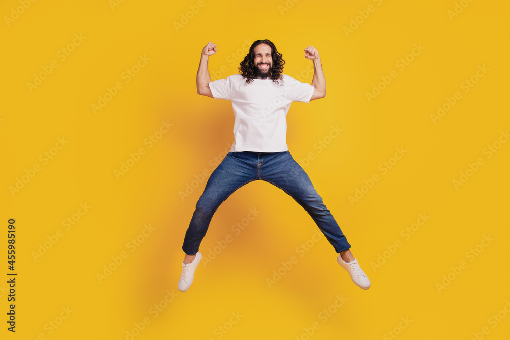 Portrait of astonished excited active guy jump hold fists on yellow background