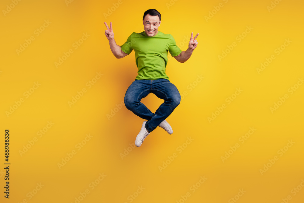 Portrait of funky cheerful friendly guy jump sport raise hand show v-sign on yellow wall