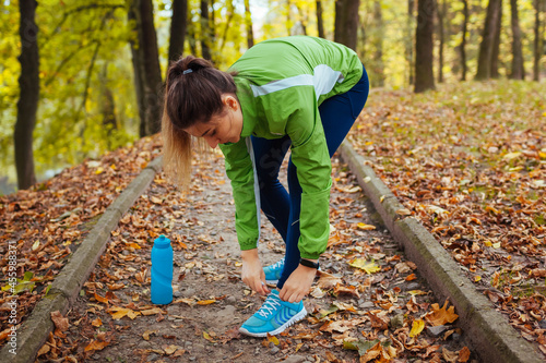 Runner tying shoe laces in autumn park. Woman training with water bottle. Active healthy sportive lifestyle