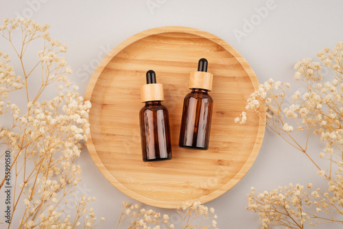 Amber glass dropper bottles different sizes with bamboo lid on wooden podium for product presentation. Top view on grey background with dry plants. Skincare product . Beauty concept for face body care
