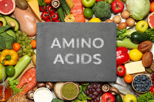 Different organic products and slate board with text AMINO ACIDS, top view
