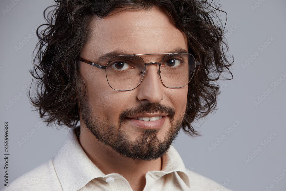 Handsome, smiling, young man with dark long hair and stylish glasses isolated on gray background, in stylish clothes, positive and success in career and business.