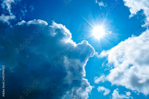 Bright sun in thick blue clouds against a blue sky.