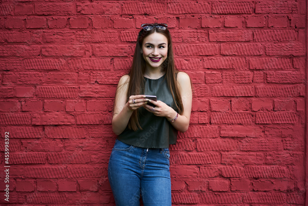Cheerful hipster girl holding cellphone gadget and smiling during leisure pastime near promotional background with copy space area, joyful female blogger with smartphone enjoying youth lifestyle Cheerful hipster girl holding cellphone gadget and smiling during leisure pastime near promotional background with copy space area, joyful female blogger with smartphone enjoying youth lifestyle