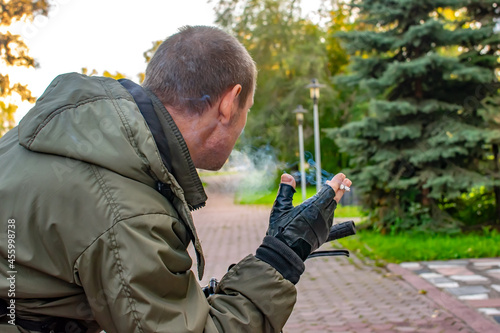 the hand of a thoughtful man holds a smoking cigarette, which stands on the road of the city alley of the park, a view from the back, rear