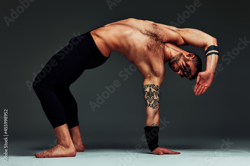 Animal instinct fitness instructor sportsman showing his incredible flexibility with an animal flow move in studio against a gray background photo