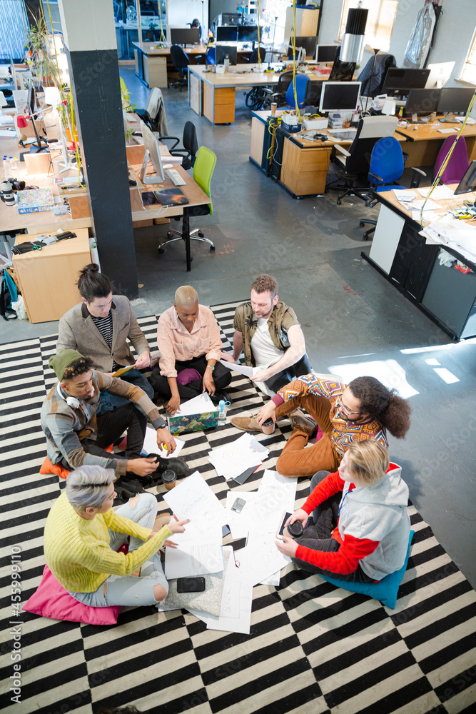 Team sitting on office floor, discussing paperwork Team sitting on office floor, discussing paperwork