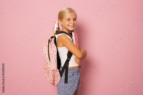 Little schoolgirl holding books isolated over pink background