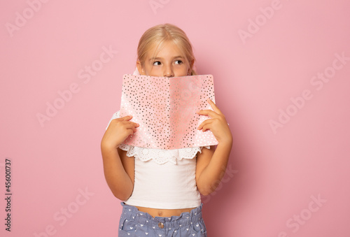 Beautiful girl with bond hair holds a notebook, picture isolated on pink background