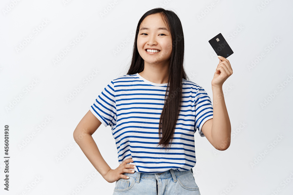 Happy asian woman raising hand and showing credit card, smiling confident, paying for something, buying, standing over white background Happy asian woman raising hand and showing credit card, smiling confident, paying for something, buying, standing over white background