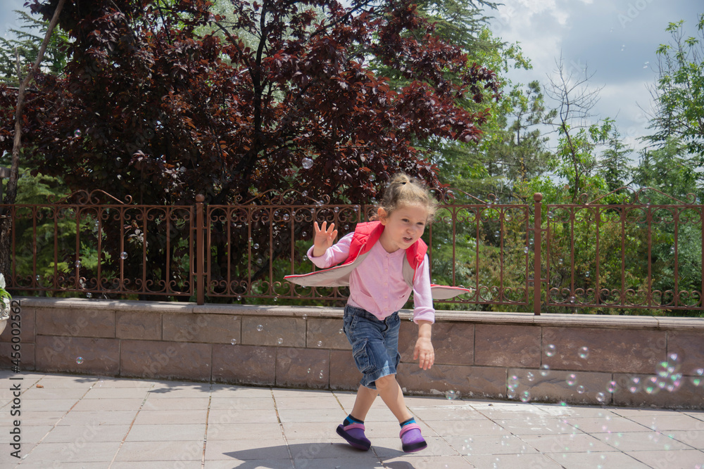 The little girl is in the garden of her house, trying to catch the bubbles. selective focus girl.
