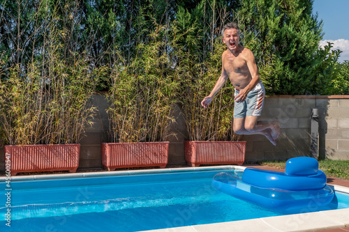 Middle-aged white man dives into a pool, cannonball style, while screaming like crazy and jumping over an airbed