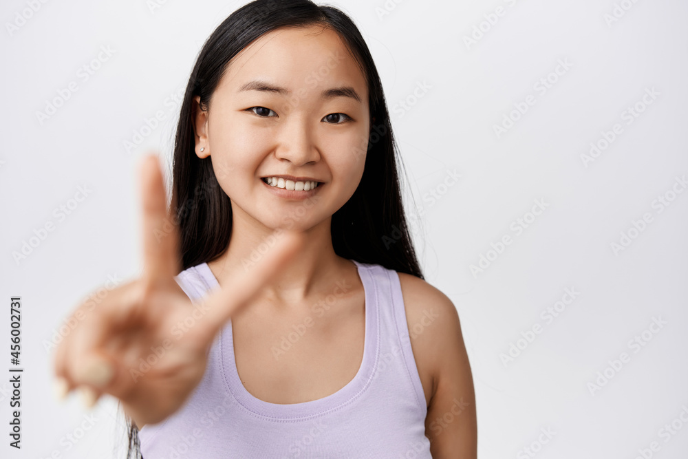 Skin care and women wellbeing. Happy asian girl without makeup, showing peace v-sign, smiling and looking cheerful at camera, white background Skin care and women wellbeing. Happy asian girl without makeup, showing peace v-sign, smiling and looking cheerful at camera, white background