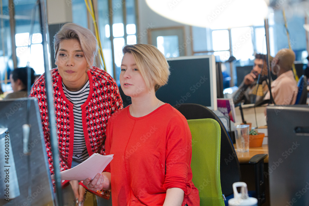 Young women discussing paperwork at computer