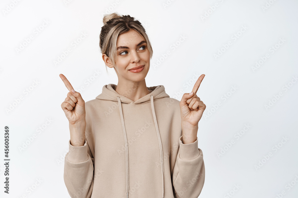 Smiling blond girl makes choice between two variants, looking at one option with pleased determined face, stands against white background Smiling blond girl makes choice between two variants, looking at one option with pleased determined face, stands against white background