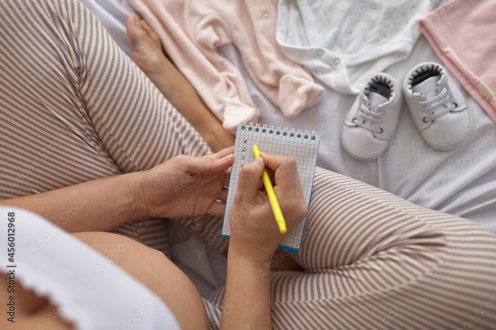 Fototapeta premium Top view of pregnant woman in the bed preparing baby clothes at home