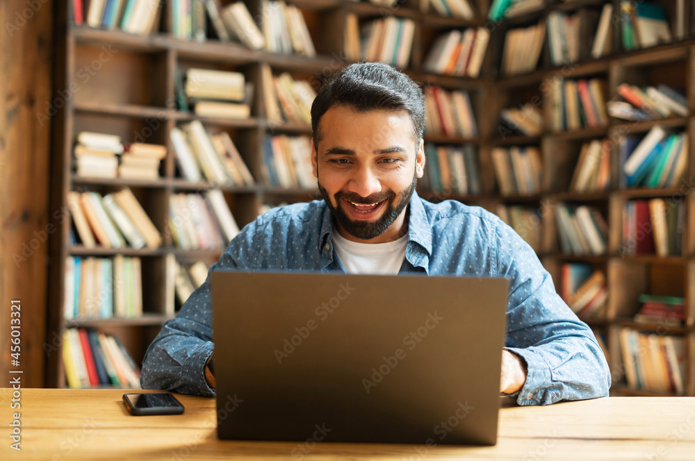 Surprised positive smiling Indian freelancer guy using laptop sitting at office or library, amazed multiracial eastern male employee received good deal or notification Surprised positive smiling Indian freelancer guy using laptop sitting at office or library, amazed multiracial eastern male employee received good deal or notification