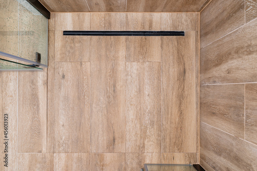 Modern black linear drain in a bathroom lined with ceramic tiles imitating wood, top view.