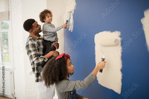 Fototapeta Naklejka Na Ścianę i Meble -  Happy father and children with paint rollers painting room