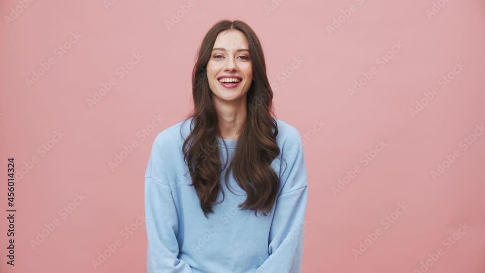 A positive brunette woman wearing hoodie nodding to the camera standing isolated over pink background in the studio A positive brunette woman wearing hoodie nodding to the camera standing isolated over pink background in the studio