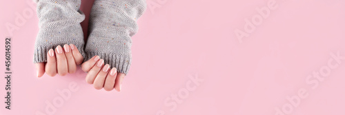 Female hands in gray knitted sweater with beautiful manicure - pink nude nails on pink background, wide panoramic banner with copy space. Nail care concept