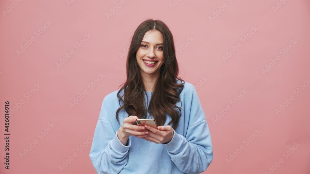 A smiling brunette woman using her mobile isolated over pink background in the studio A smiling brunette woman using her mobile isolated over pink background in the studio