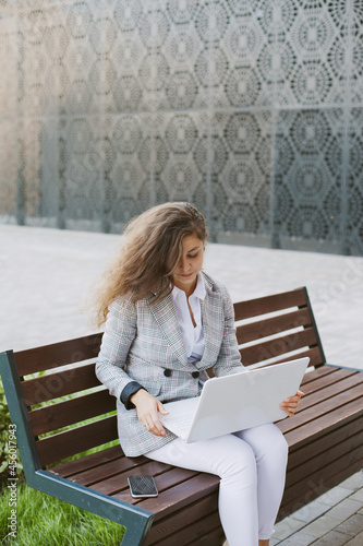 Woman working on laptop sitting on abench near modern office building photo