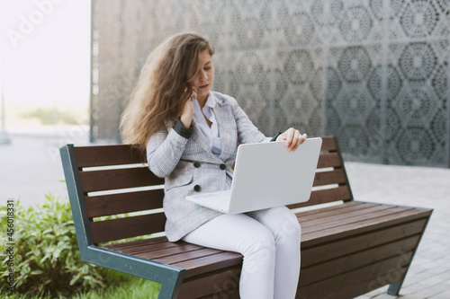 Woman working on laptop sitting on abench near modern office building photo