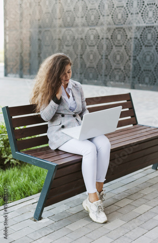 Woman working on laptop sitting on abench near modern office building photo