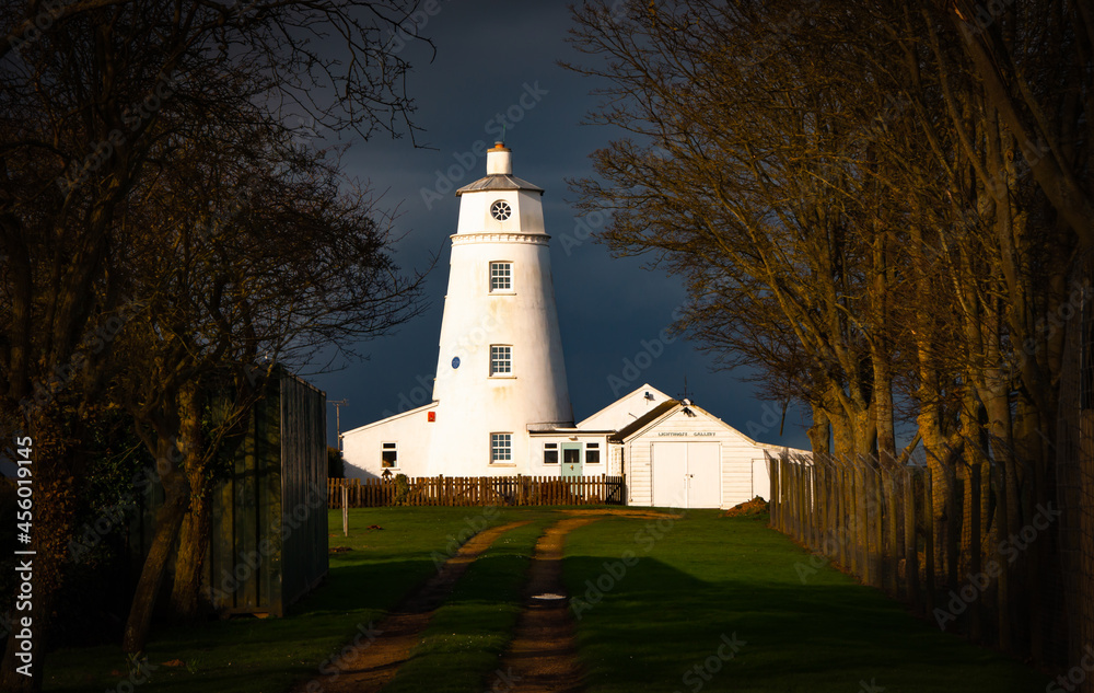 Winter sunlight falling on East Bank Lighthouse famous for The Snow Goose, against a stormy sky in Sutton Bridge, River Nene, Spalding, Lincolnshire
