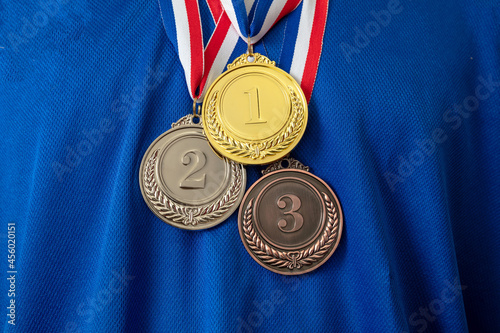 Gold, silver and bronze medals set on blue shirt background. Sports athletes winners prize