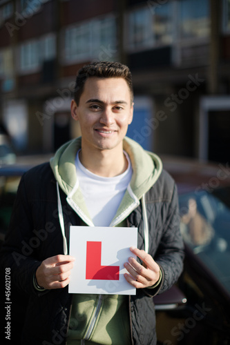 Portrait confident, happy young man holding learners permit by car