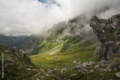 Collado del Frade en Picos de Europa. Idílico paisaje de montaña con cabaña en el centro rodeada de verdes prados con nubes alrededor de la montaña