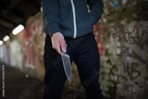 Dangerous man in hoody holding knife weapon in urban tunnel