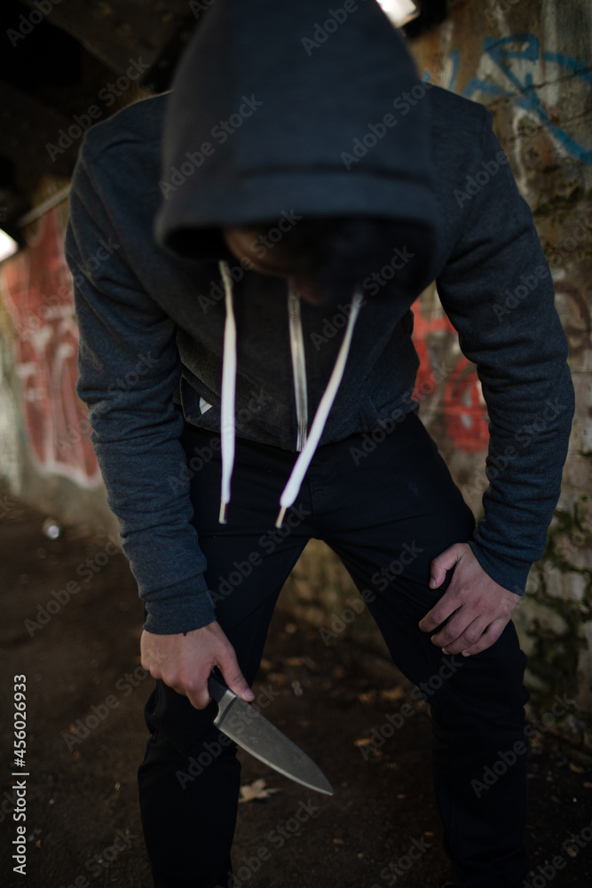 Dangerous man in hoody holding knife weapon in urban tunnel Dangerous man in hoody holding knife weapon in urban tunnel