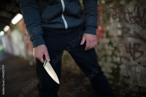 Dangerous man in hoody holding knife weapon in urban tunnel