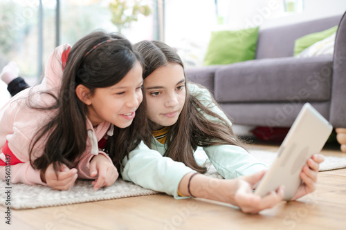 Portrait smiling sisters using digital tablet camera on living room floor