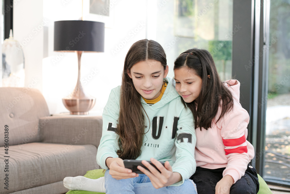 Playful sisters taking selfie with smart phone in living room Playful sisters taking selfie with smart phone in living room