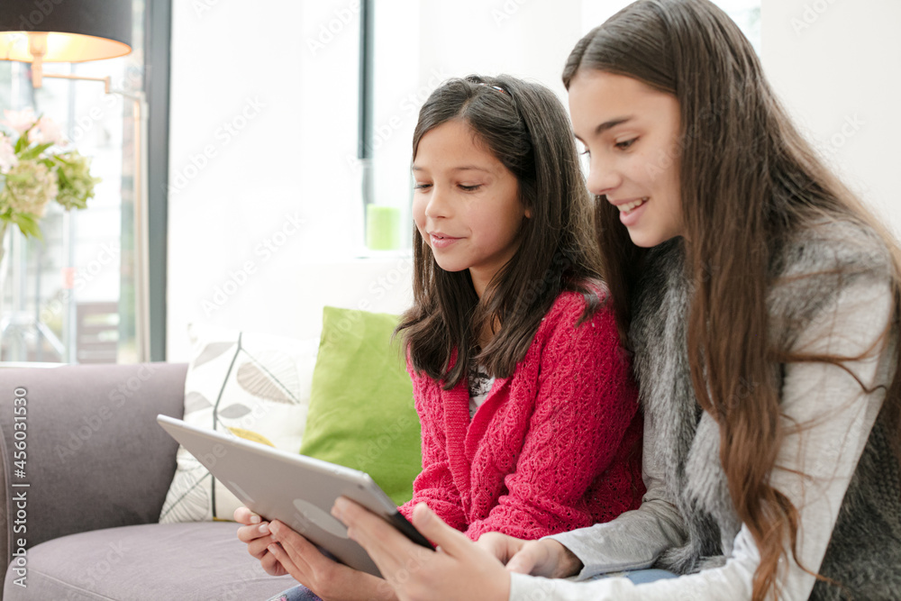 Happy sisters using digital tablet on living room sofa Happy sisters using digital tablet on living room sofa