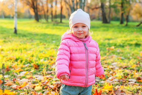 Happy young girl smiling in beautiful autumn park on nature walks outdoors. Little child playing in autumn fall orange yellow background. Hello autumn concept.