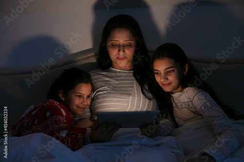 Surprised mother and daughters watching movie on digital tablet in dark bedroom