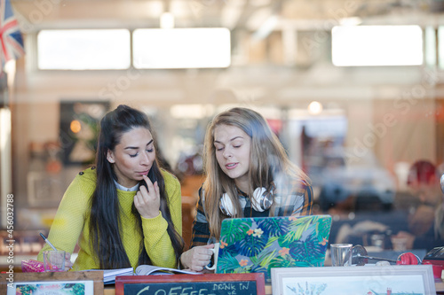 Young female college students studying at laptop in cafe window