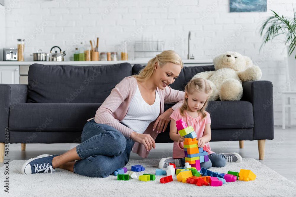 girl making tower of building blocks near mom and teddy bear on couch girl making tower of building blocks near mom and teddy bear on couch