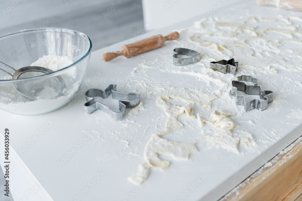 glass bowl, sieve, cookie cutters and rolling pin on white table with scattered flour glass bowl, sieve, cookie cutters and rolling pin on white table with scattered flour